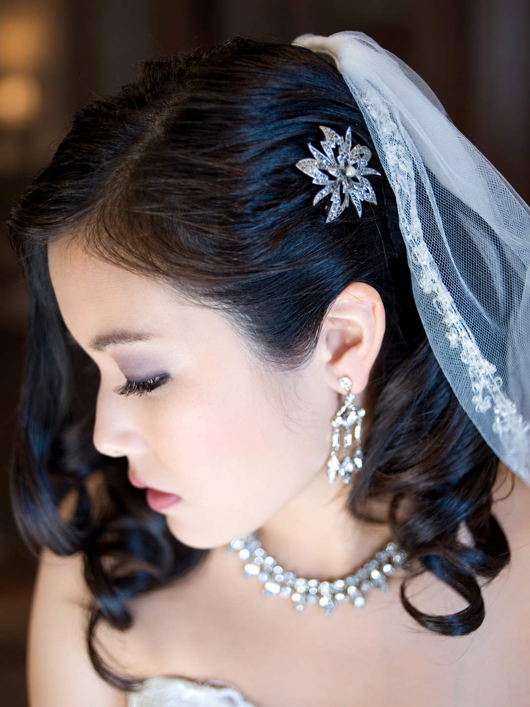 My soft bridal makeup and dark curls with a crystal hair comb and veil, seen in profile.