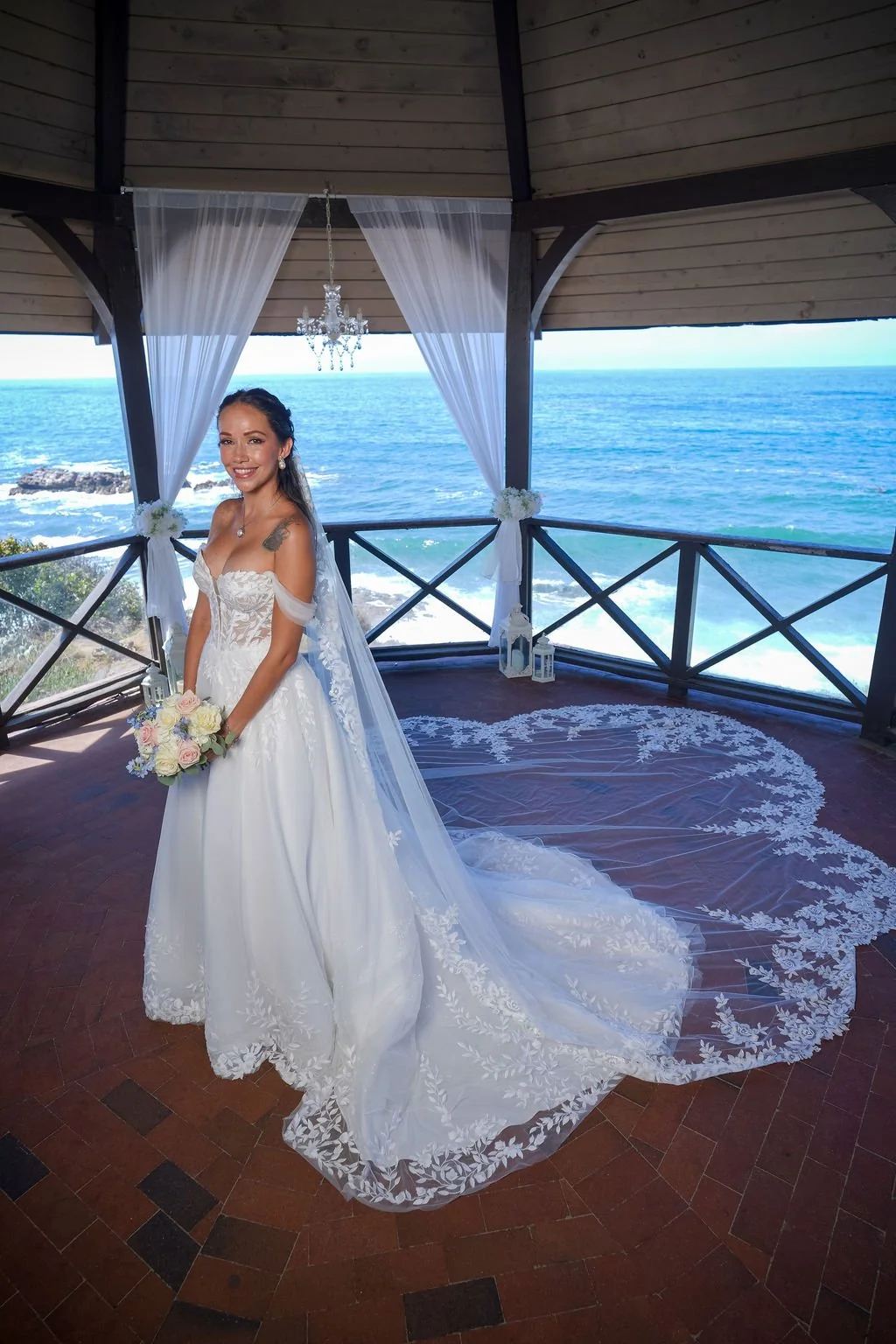 My bridal hair and makeup on Grace, smiling with her bouquet beside the ocean in Laguna Beach.